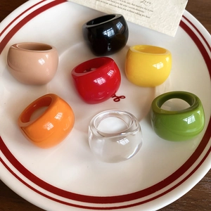 Set of seven colorful oval resin rings in warm tones displayed on a white ceramic plate