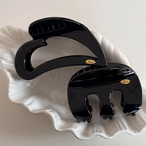 Detail of two black hair claws with gold Love emblem on a white ceramic leaf tray
