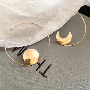 Detail of asymmetrical gold moon and sun hoop earrings on textured backdrop