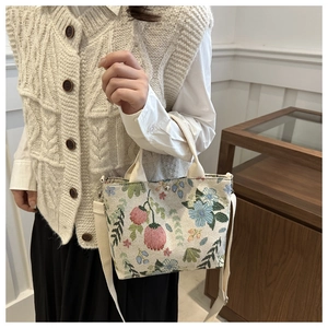 Close-up of floral embroidery detail on beige canvas handbag with shoulder strap