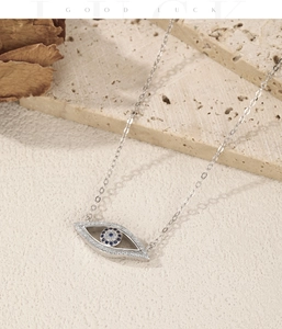Detail of S925 silver Evil Eye necklace with blue zircon on a beige stone surface
