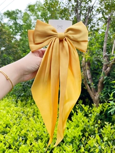 Detail of yellow satin oversized bow hair clip with elegant long ribbons on cardboard