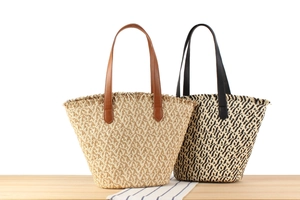Detail of woven straw tote bags with leather handles in natural and black pattern