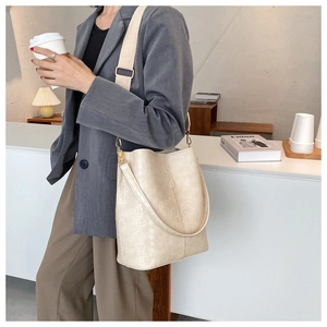 Detail of creamy crocodile pattern bucket bag with wide shoulder strap and gold hardware