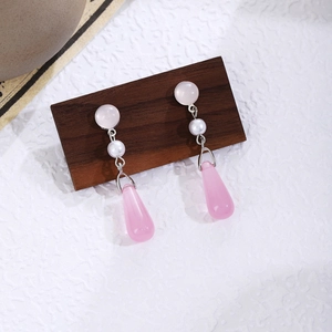 Detail of pink teardrop glass earrings with white pearls on a wooden display stand