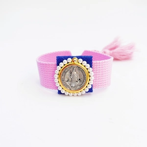 Macro shot of pink woven bracelet featuring Saint Benedict medal with gold pearl border