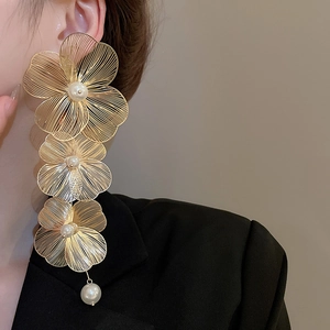 Dettaglio di orecchini a fiore traforato in oro con ciondoli di perle su una modella