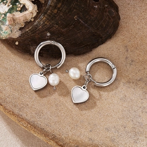 Detailed close-up of silver heart-shaped shell earrings with pearl on stone