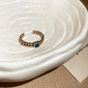 Macro detail of vintage gold chain ring featuring a square blue gemstone inlay