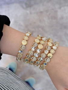 Detail of layered gold bracelets with white rhinestone smile and floral charms on wrist