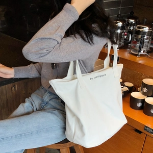 Bolso tote minimalista de lona blanca con letras negras mostrado en una acogedora cafetería