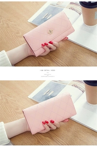 Detailed view of pink long wallet with quilted stitching and gold crown emblem on wood