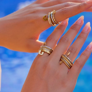 Detail of stacked silver and gold safety pin rings worn on hand against blue water