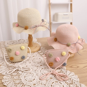 Detailed view of straw sun hat and matching mini bag with colorful pom-pom trim