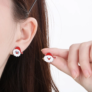 Detail shot of Santa Claus enamel earrings in red and white on ear and held by hand