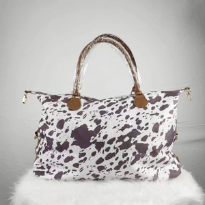 Close-up of cow print canvas weekender bag with brown handles and gold hardware