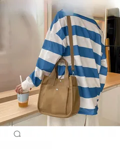 Brown canvas handbag with double front pockets and adjustable shoulder strap in casual setting