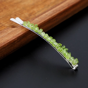 Close-up of small silver hair clip with natural green crystal stones on a wood tray