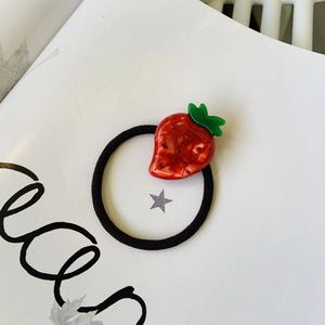 Close-up of red strawberry hair tie with shiny rhinestones and green leaf detail