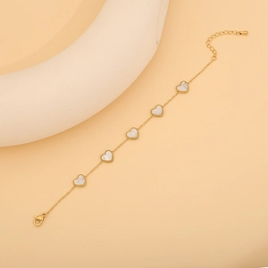 Détail d'un bracelet doré avec cinq breloques en forme de cœur blanc et fermoir réglable