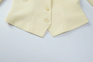 Detailed close-up of light yellow blazer hem with two resin buttons and woven texture