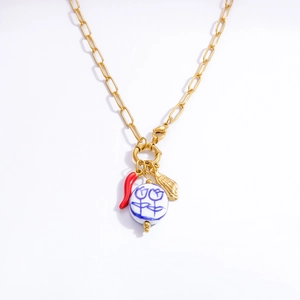 Detailed shot of golden paperclip necklace featuring chili and shell pendants