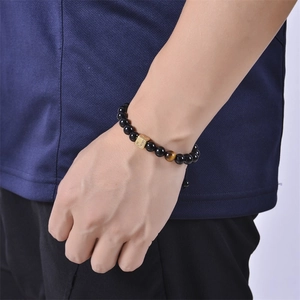 Detail of male model wearing a black onyx and tiger eye stone bracelet with letter G charm