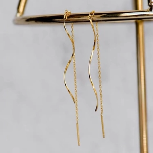 Détail de boucles d'oreilles traversantes dorées avec vagues et pompons sur marbre