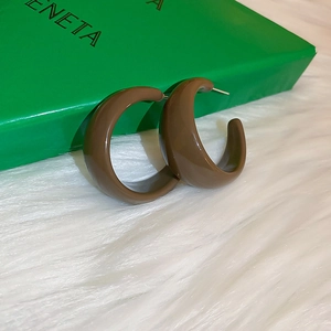 Detailed macro view of brown resin C-shape hoop earrings on white plush background