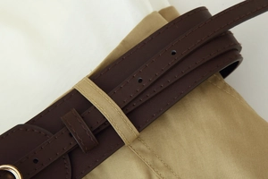 Détail d'une ceinture en cuir marron foncé avec double couture sur une robe kaki