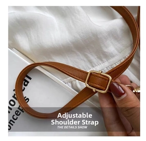 Detail of adjustable brown leather shoulder strap with gold buckle on straw bucket bag