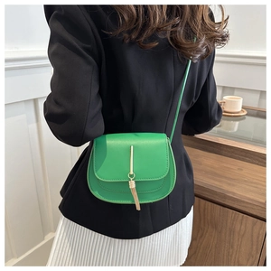 Detail of vibrant green leather saddle bag with golden tassel buckle on a model