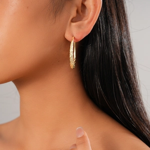Close-up of gold geometric twisted hoop earring featuring detailed braided texture on model
