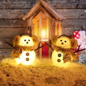 Pair of glowing Christmas snowmen with plaid scarves on snow with warm festive lighting