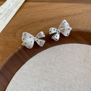 Detail of silver bow earrings with brushed texture and tiny zircon inlay on wood edge