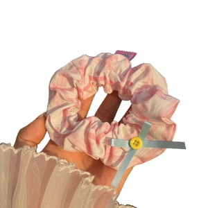 Pink checkered scrunchie with blue ribbon bow and yellow button detail in hand