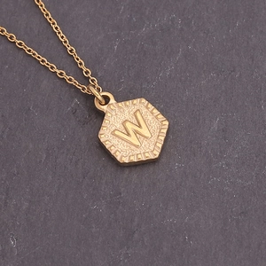 Close-up of golden necklace featuring a hexagonal shield pendant with embossed letter W