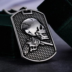 Macro shot of silver skull and revolver pistol pendant on dark green velvet box