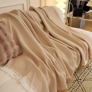 Beige waffle weave sofa cover with decorative fringe tassels on a modern couch