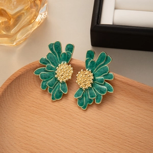 Detailed view of emerald green daisy earrings with golden center on wood tray