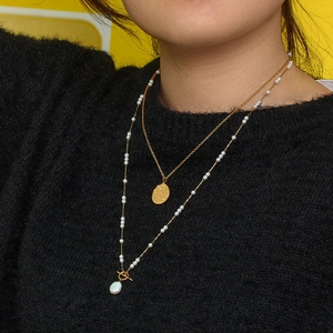 Close-up of layered gold necklaces with zircon round pendant and baroque pearl toggle clasp