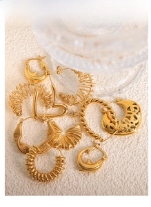 Macro detail of various 18k gold plated hollow titanium steel earrings on textured surface