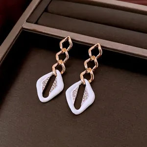 Luxury geometric drop earrings with gold chains, white enamel, and crystal inlay