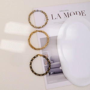 Three Byzantine chain bracelets in gold, silver and black finishes on a Nordic style background
