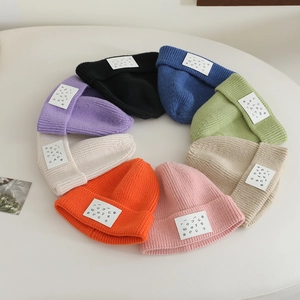 Overhead view of ribbed knit beanies in 8 candy colors with letter patch details