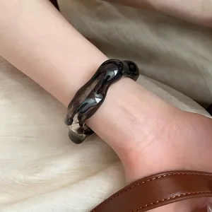 Close-up of translucent dark grey acrylic bangle with irregular wave texture on model