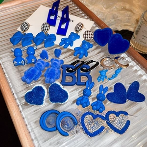 Detailed close-up of blue flocked bear and heart earrings in a clear striped tray
