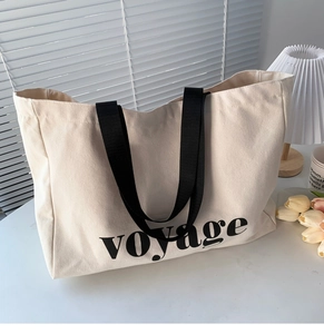 Detail of canvas tote bag with black voyage text and fabric shoulder strap in beige