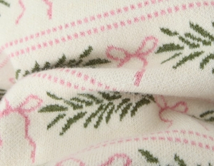 Detailed macro view of cream knit fabric featuring pink bow and green pine jacquard pattern