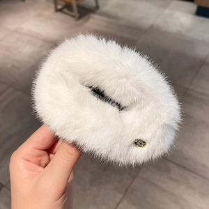 Close-up of white plush round hair clip showing soft faux fur texture and gold detail